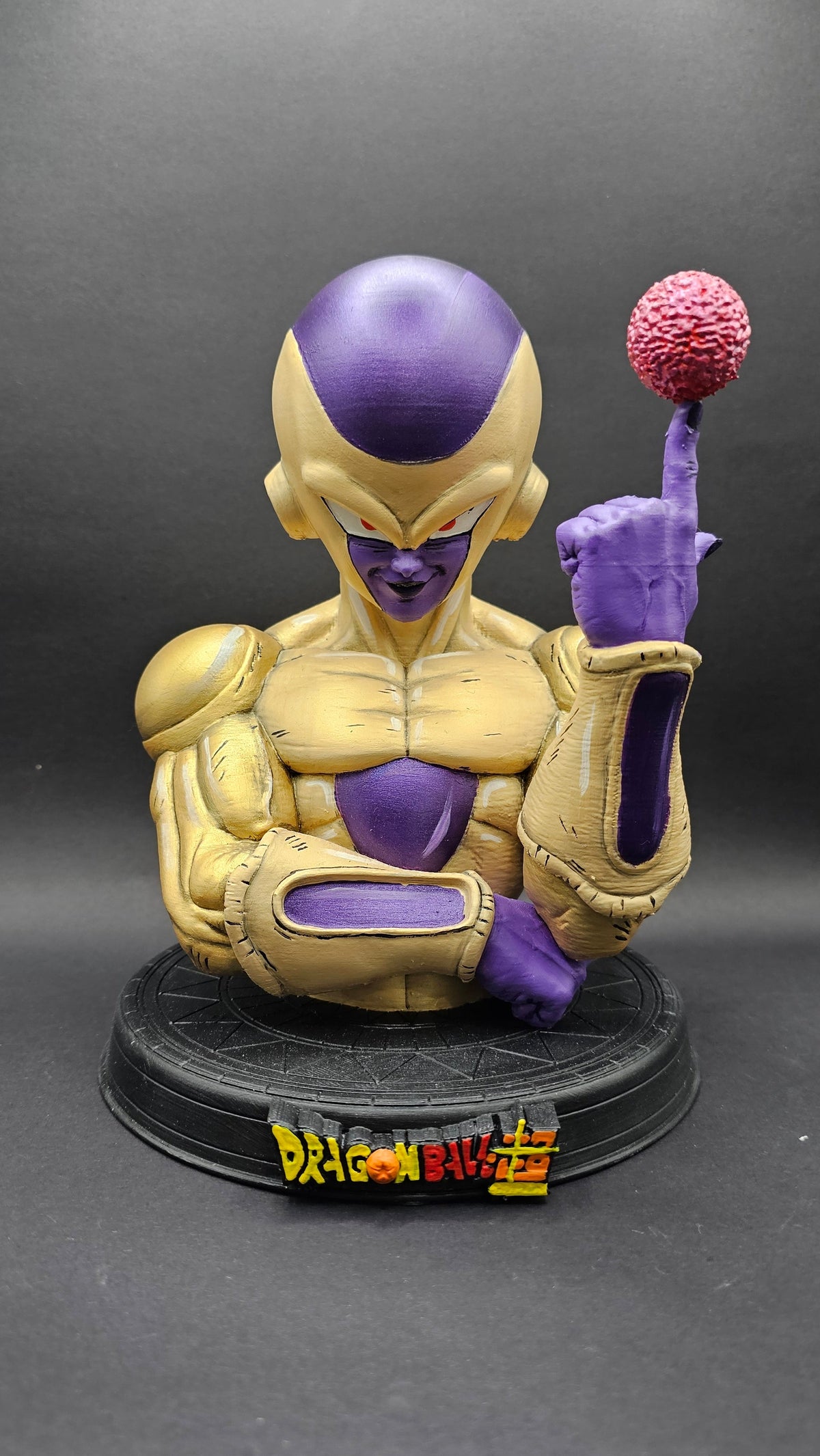 A collectible bust statue of the Dragon Ball character Frieza, featuring his signature purple skin and gold armor, holding a pink brain on a finger, mounted on a black circular base with a 'Dragon Ball' logo.